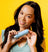 Smiling woman holding a blue Meridian grooming product bottle against a bright yellow background.