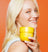 Smiling blonde hair woman holding a yellow container of skincare pads against an orange background.