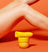 Yellow electric hair trimmer and a container of exfoliating pads placed against a vibrant orange background with smooth legs in the frame.