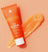 Orange tube of grooming exfoliator scrub labeled "The Scrub" with a smear of the exfoliating gel next to it on a matching orange background.