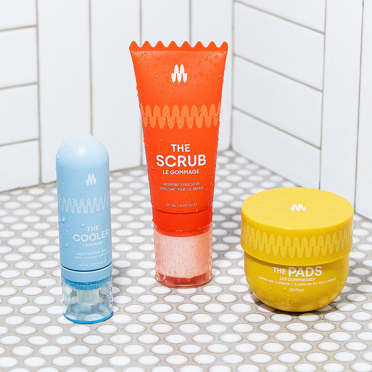Blue daily soothing spray, orange grooming exfoliator scrub tube, and yellow ingrown hair eliminator pads on white tiled floor.