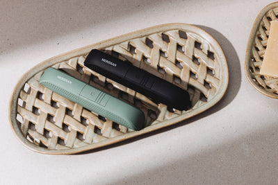 Two Meridian-branded grooming trimmers, one black and one green, resting on a textured ceramic tray.