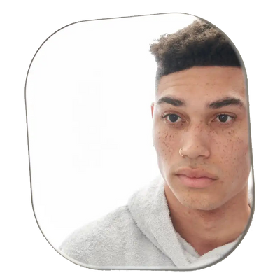 Young man with freckles and a nose ring looking at his reflection in a mirror while wearing a gray towel.