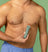 Man with chest hair holding green electric body hair trimmer against bare chest, grooming and personal care tool.