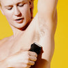 Man trimming underarm hair with electric trimmer against bright yellow background for personal grooming.