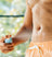 Man wearing orange swim trunks applying sunscreen spray to torso, summer skincare, sun protection outdoors