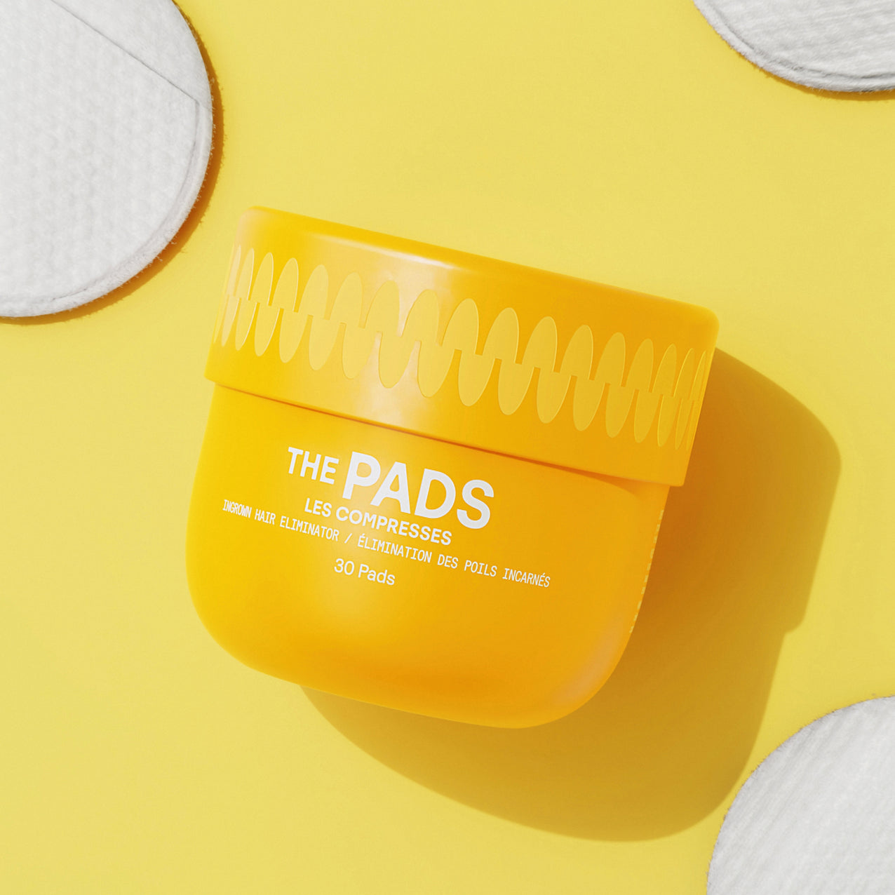 Yellow container of "The Pads" facial exfoliating pads with cotton pads on a bright yellow background.