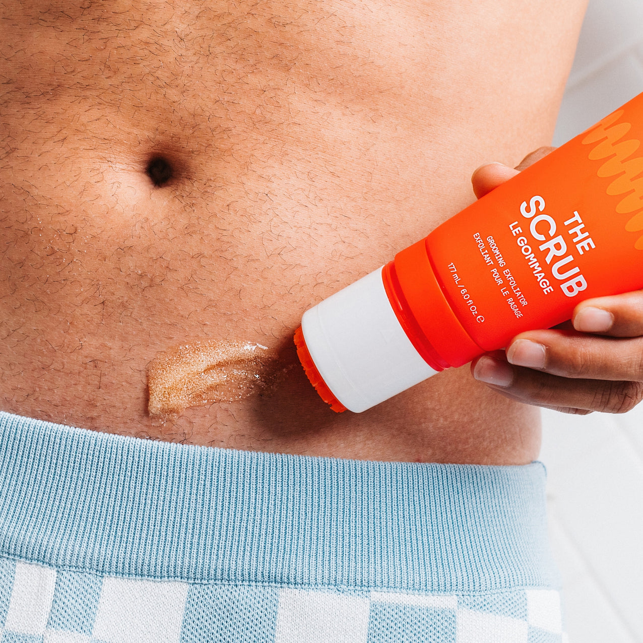 Exfoliating body scrub cream being applied on abdomen, skincare product for smooth, healthy skin, men's grooming routine.