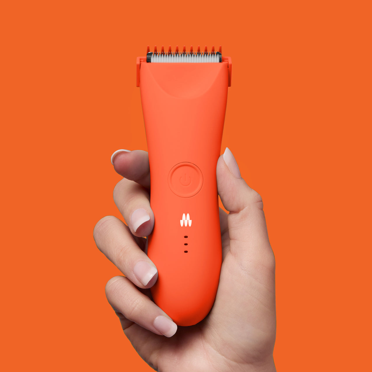 Orange cordless hair clipper with power button and LED indicators held by hand against orange background.