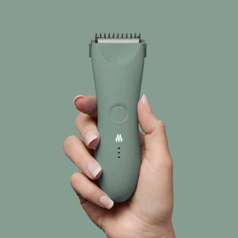 Compact sage green electric hair clipper with power button and LED indicators held by hand on matching green background