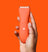 Hand holding a sleek orange cordless hair clipper with power button and LED battery indicators on a matching orange background.
