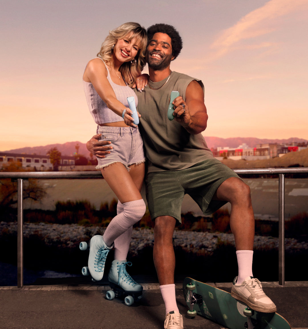 Young couple roller skating together outdoors at sunset with cityscape and mountains in the background, wearing casual sporty outfits.